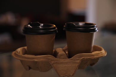 Takeaway coffee cups with cardboard holder on glass table indoors, closeup