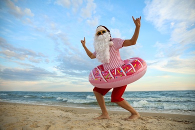 Photo of Santa Claus with inflatable ring having fun on beach, space for text. Christmas vacation