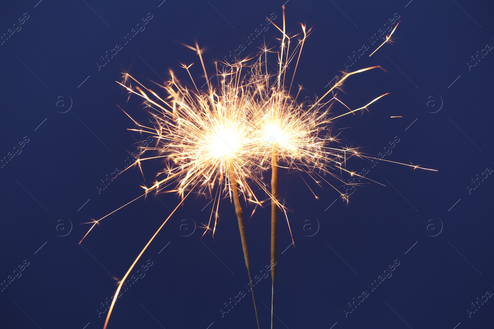 Photo of Bright burning sparkler on blue background, closeup