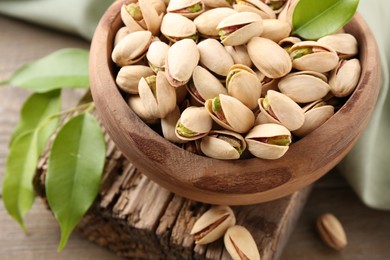 Photo of Delicious pistachios in bowl on wooden table, closeup