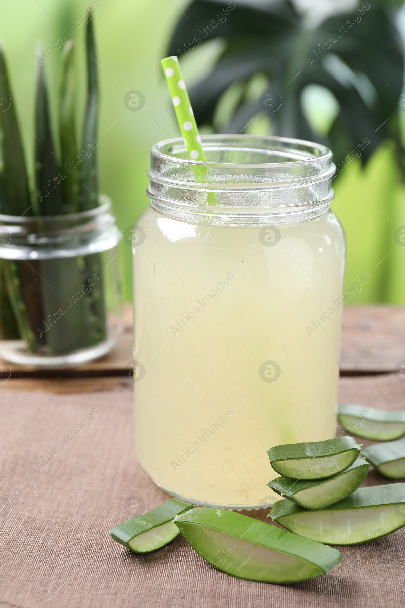 Photo of Fresh aloe juice in jar with straw and cut leaves on wooden table outdoors, closeup