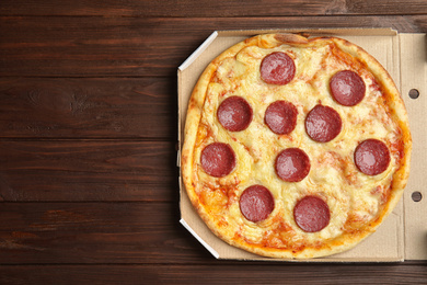 Photo of Tasty pepperoni pizza in cardboard box on wooden table, top view. Space for text