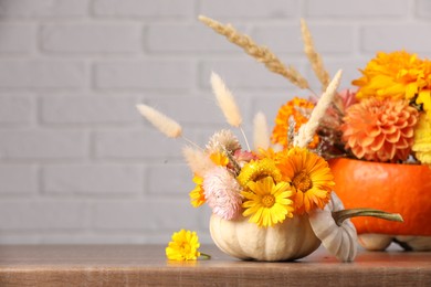 Photo of Decorative pumpkins with beautiful flowers and spikelets on wooden table against white brick wall, closeup. Space for text