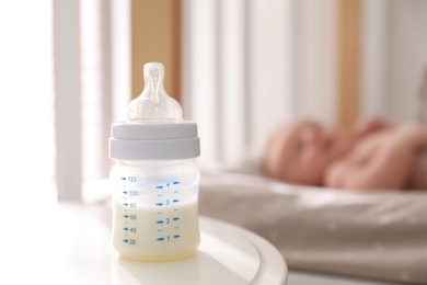 Photo of Healthy baby sleeping in cot, focus on bottle with milk