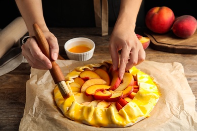 Photo of Woman making peach pie at wooden table, closeup