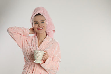 Beautiful young woman in bathrobe with cup of coffee on light background. Space for text