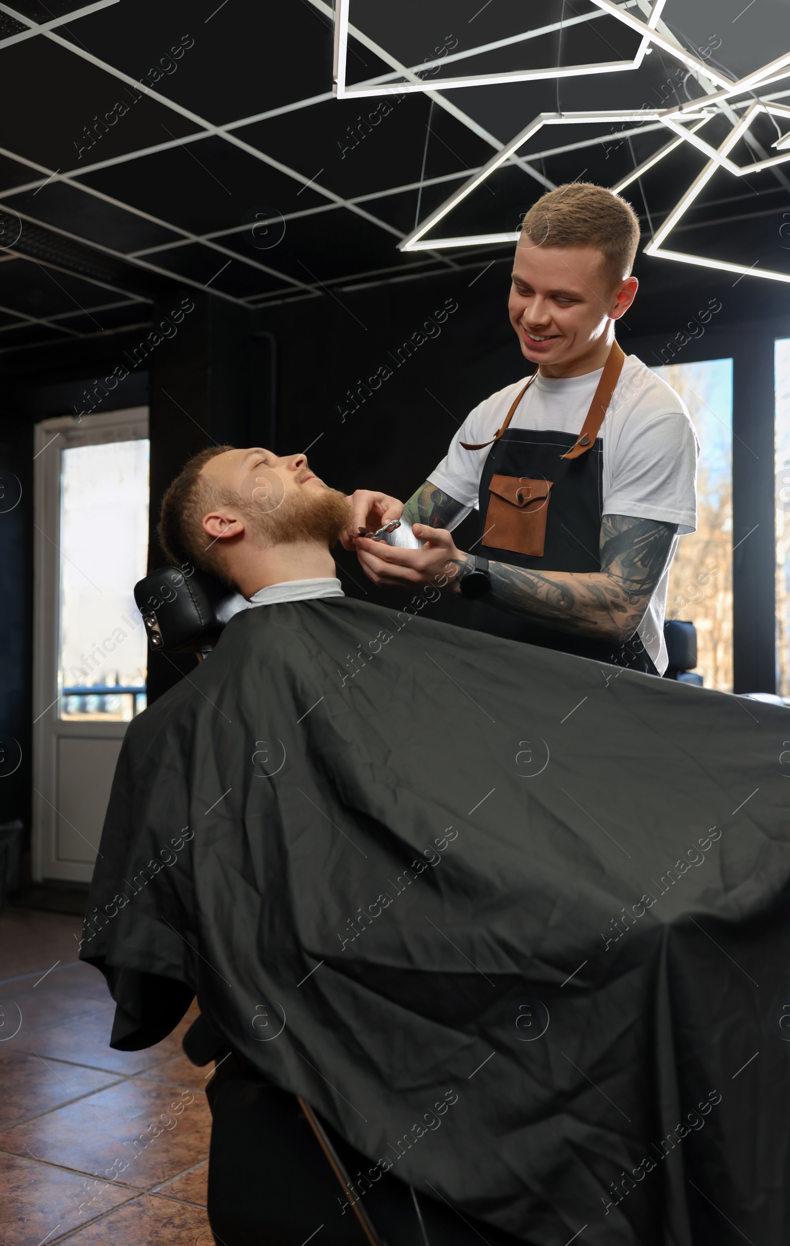 Photo of Professional hairdresser working with bearded client in barbershop