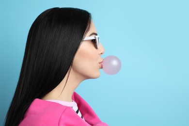 Fashionable young woman blowing bubblegum on light blue background, space for text