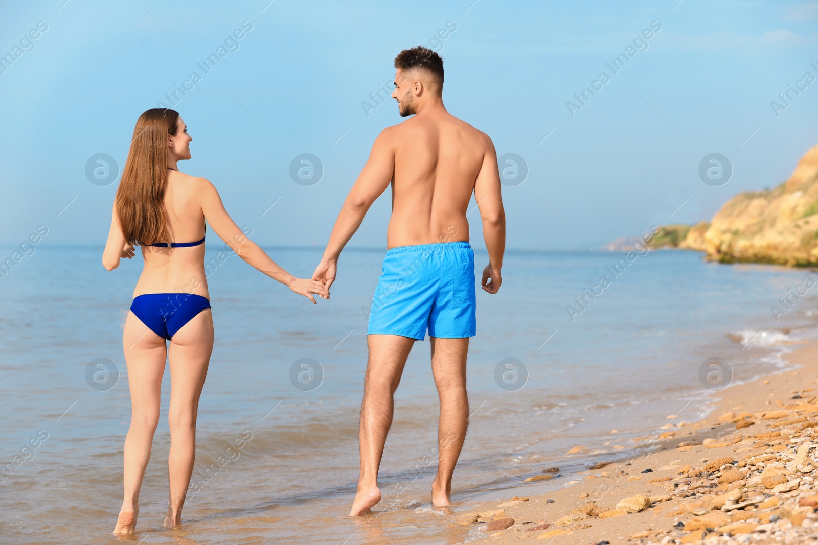 Photo of Young woman in bikini with her boyfriend walking on beach, space for text. Lovely couple