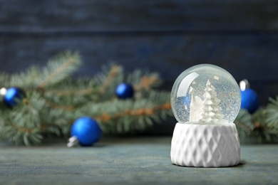 Snow globe with deer and trees on blue wooden table, space for text. Christmas season