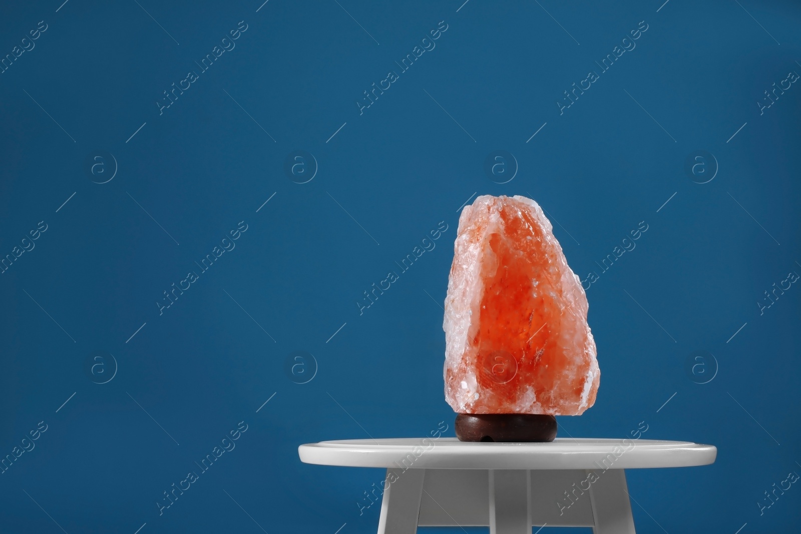 Photo of Himalayan salt lamp on white table against blue background. Space for text