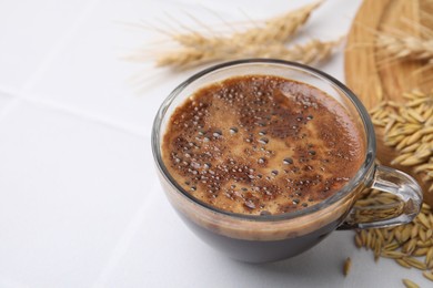 Cup of barley coffee, grains and spikes on white table, closeup. Space for text