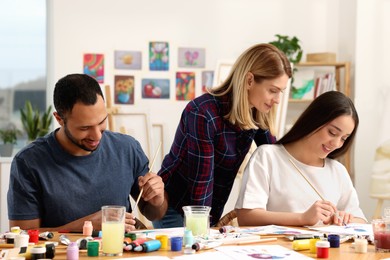 Photo of Artist teaching her students to paint at table in studio. Creative hobby
