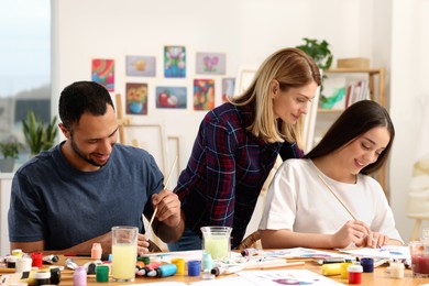 Artist teaching her students to paint at table in studio. Creative hobby