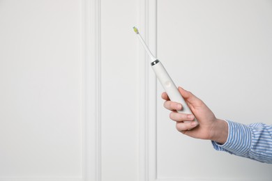 Photo of Woman holding electric toothbrush near white wall, closeup. Space for text