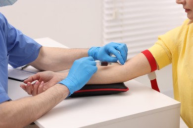 Doctor taking blood sample from patient with syringe at white table in hospital, closeup