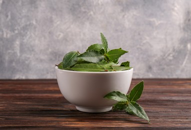 Photo of Fresh green bay leaves in bowl on wooden table