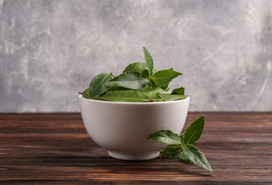 Fresh green bay leaves in bowl on wooden table