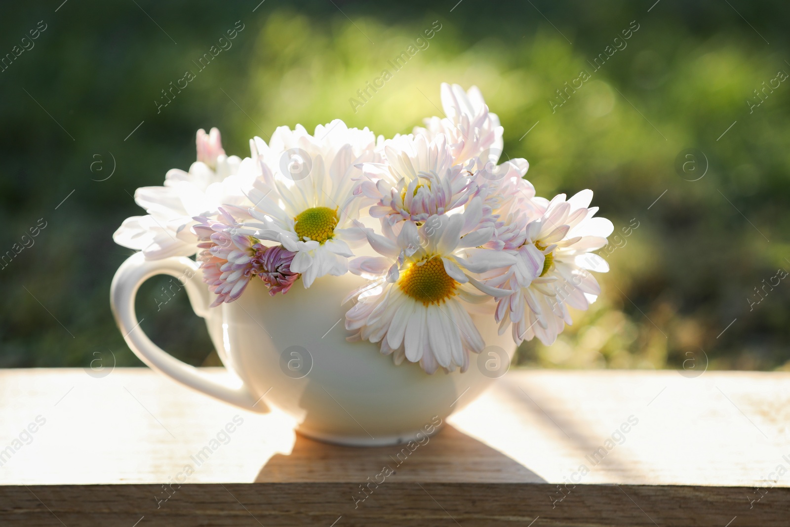 Photo of Beautiful wild flowers in cup on wooden table against blurred background, closeup