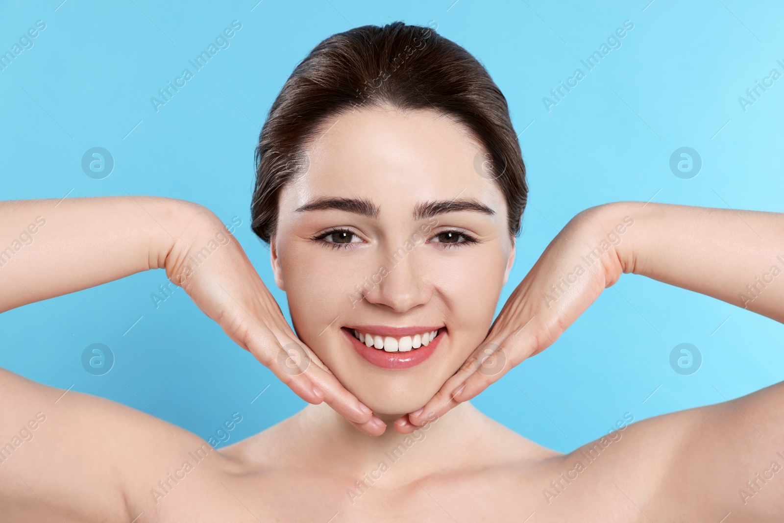 Photo of Young woman massaging her face on turquoise background