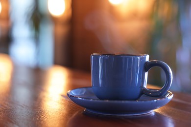 Photo of Steaming ceramic cup of coffee on wooden table in cafe. Space for text