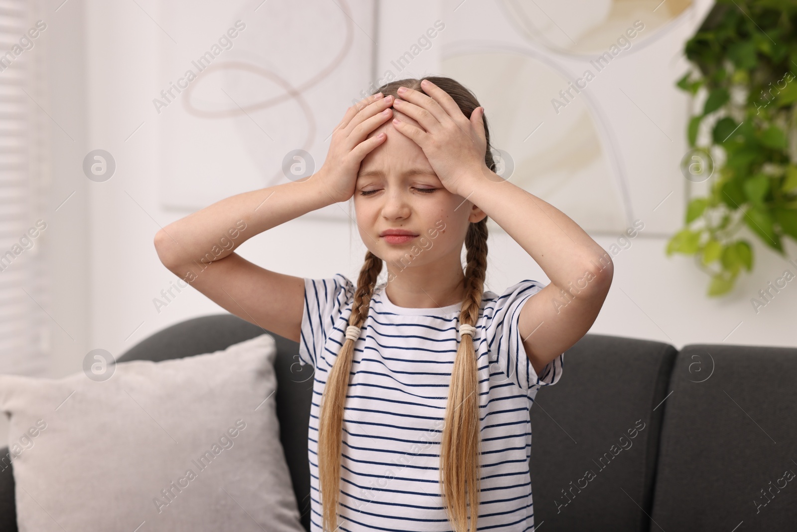 Photo of Little girl suffering from headache on sofa indoors