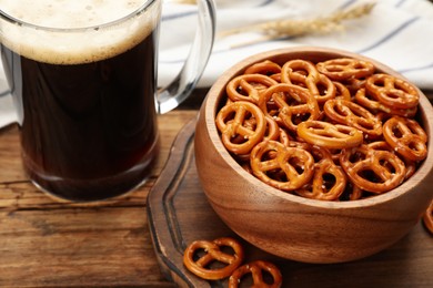 Photo of Delicious pretzel crackers and glass of beer on wooden table, closeup