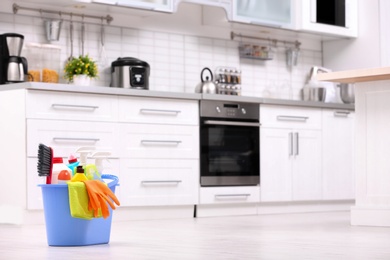 Photo of Bucket with cleaning supplies on floor in kitchen. Space for text