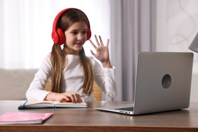 Photo of E-learning. Cute girl raising her hand to answer during online lesson at table indoors, selective focus