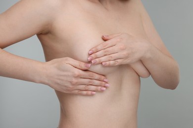 Photo of Mammology. Naked young woman doing breast self-examination on light grey background, closeup