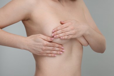 Mammology. Naked young woman doing breast self-examination on light grey background, closeup