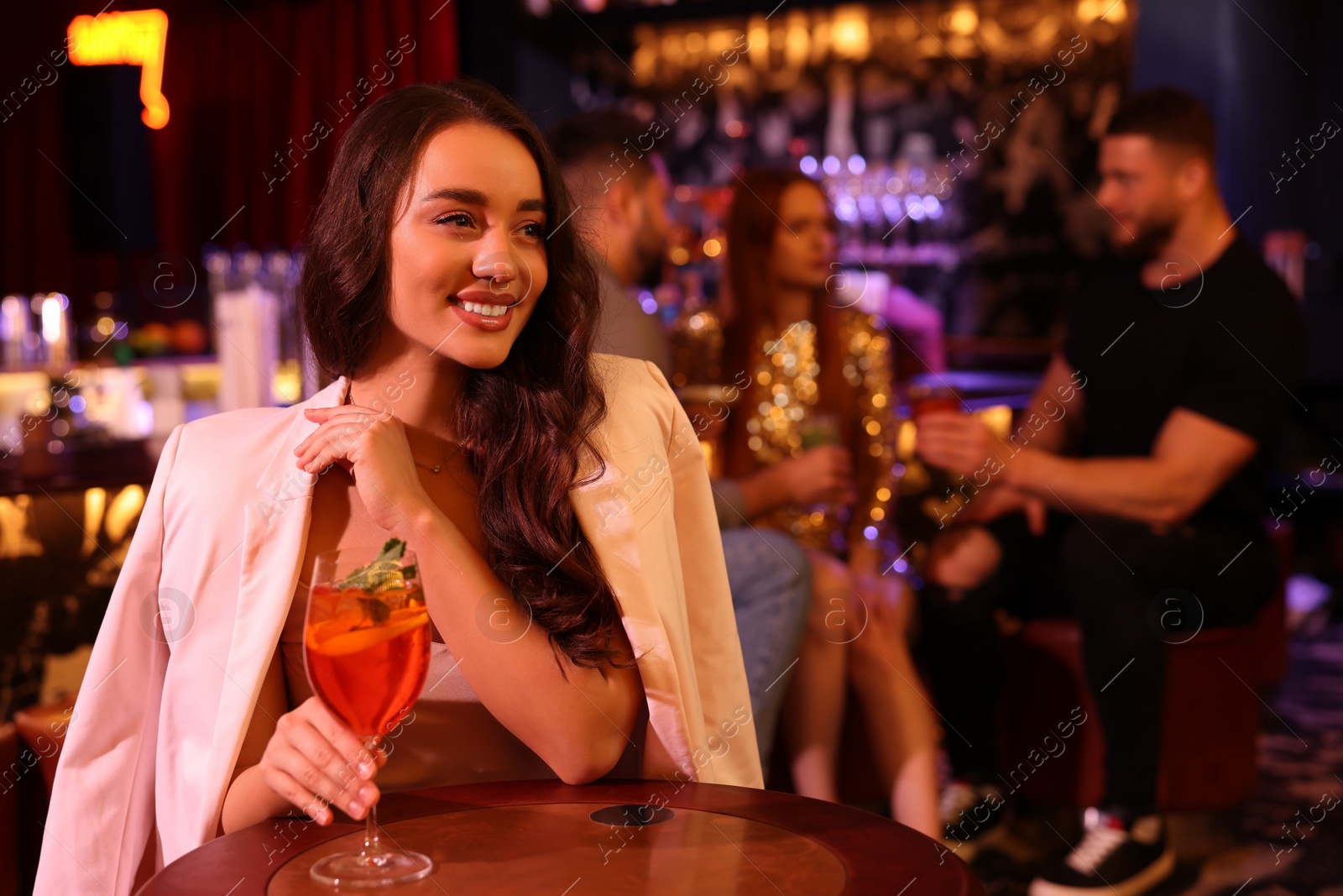 Photo of Friends spending time together in bar. Beautiful woman with fresh alcoholic cocktail at table, space for text