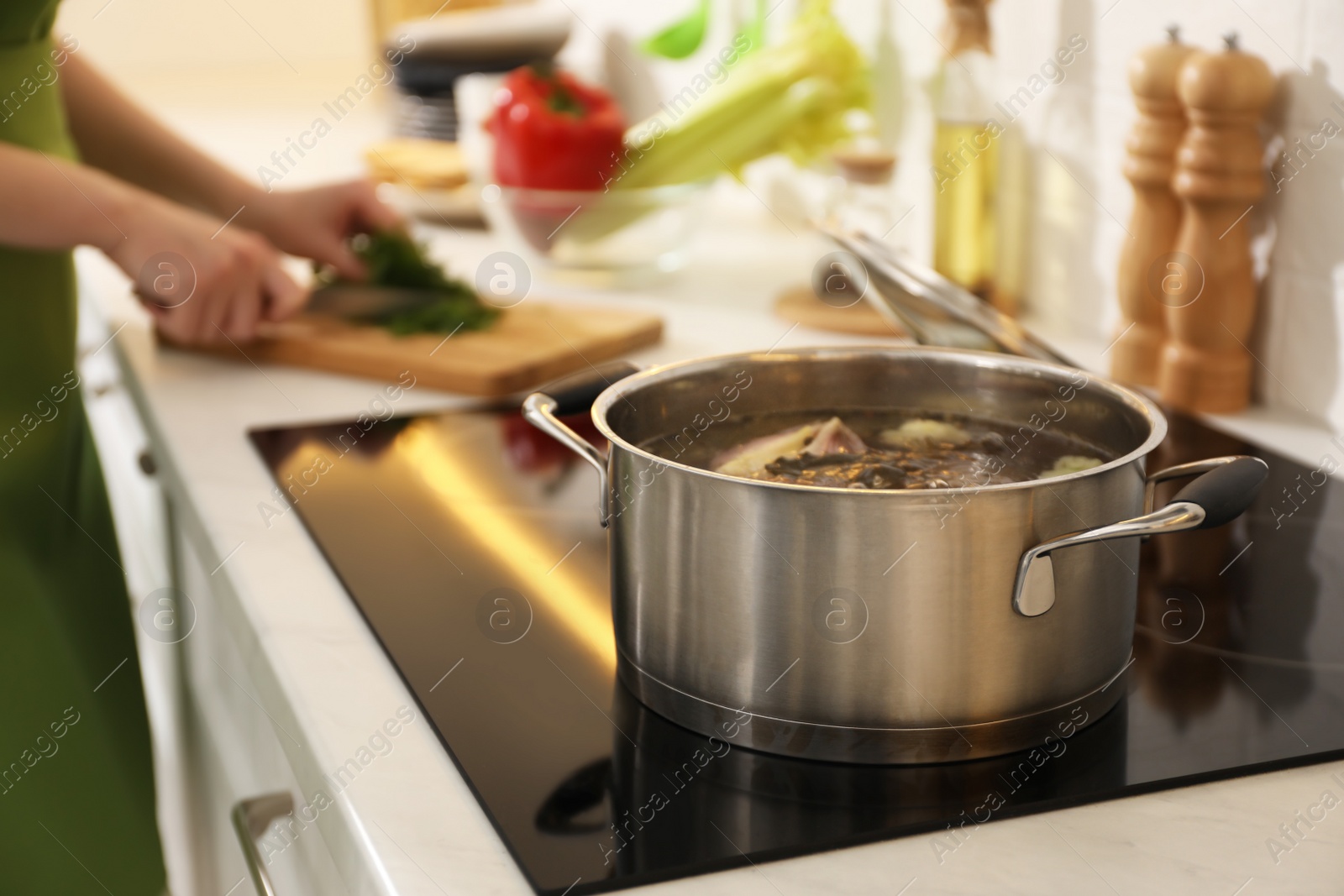 Photo of Homemade bouillon recipe. Woman cutting greenery in kitchen, focus on pot