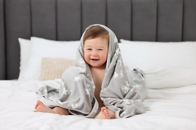 Photo of Happy baby boy with blanket sitting on bed at home