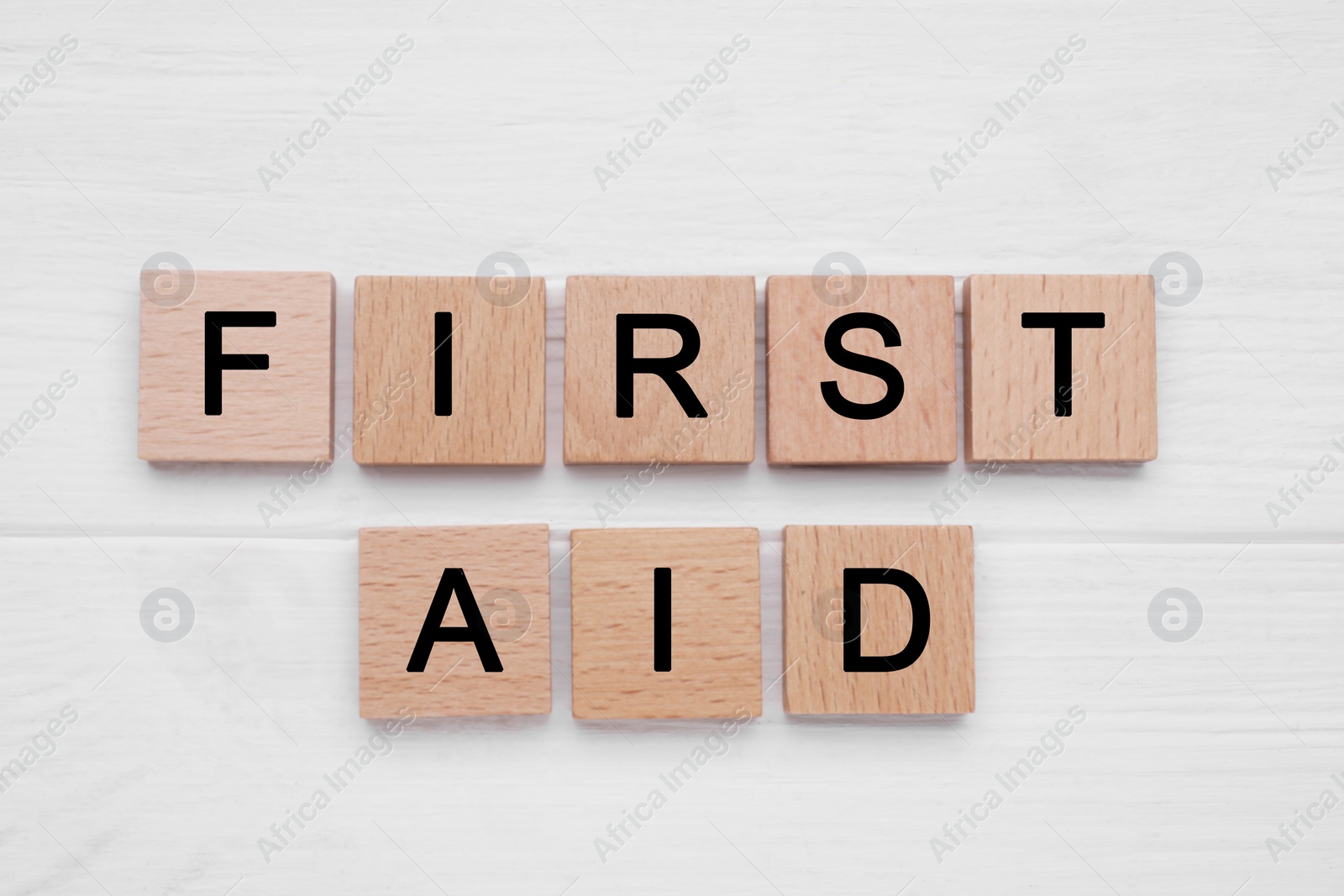 Photo of Words First Aid made of cubes on white wooden table, flat lay