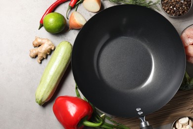 Empty iron wok and raw ingredients on grey table, flat lay