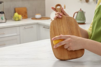 Woman rubbing wooden cutting board with lemon at white table in kitchen, closeup. Space for text