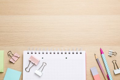 Photo of Binder clips and other stationery on wooden background, flat lay. Space for text