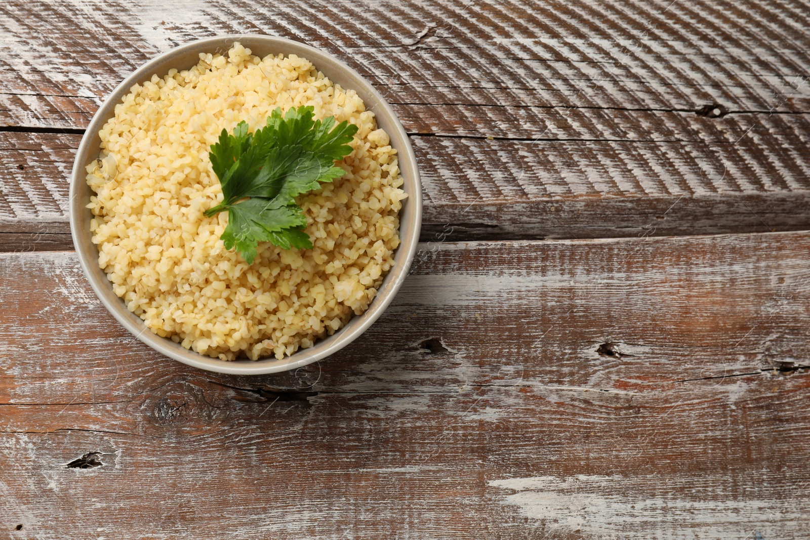 Photo of Delicious bulgur and parsley in bowl on wooden table, top view. Space for text