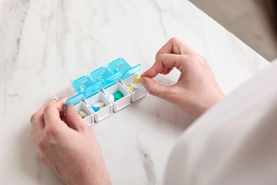 Woman with pills and organizer at white marble table, closeup