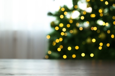 Photo of Blurred view of fir tree with glowing Christmas lights near table indoors