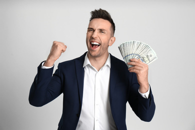 Emotional man with cash money on light grey background