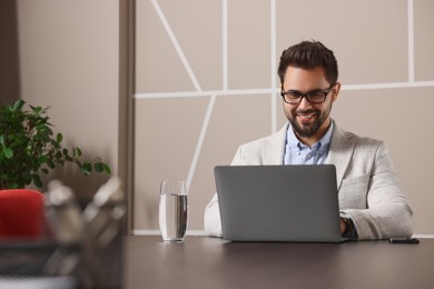 Photo of Happy young man with glasses working on laptop at table in office. Space for text