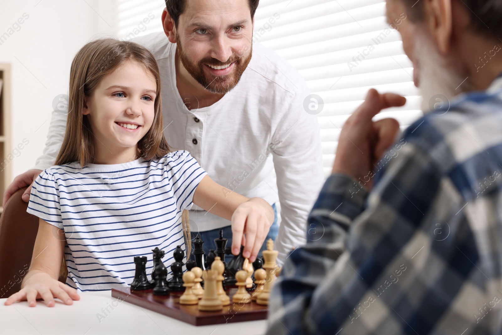 Photo of Family playing chess together at table in room