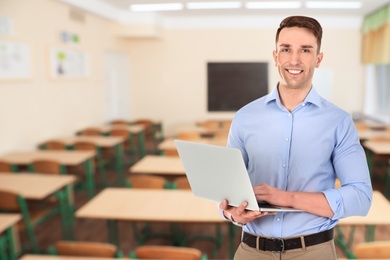 Image of Young teacher with laptop waiting for students in classroom