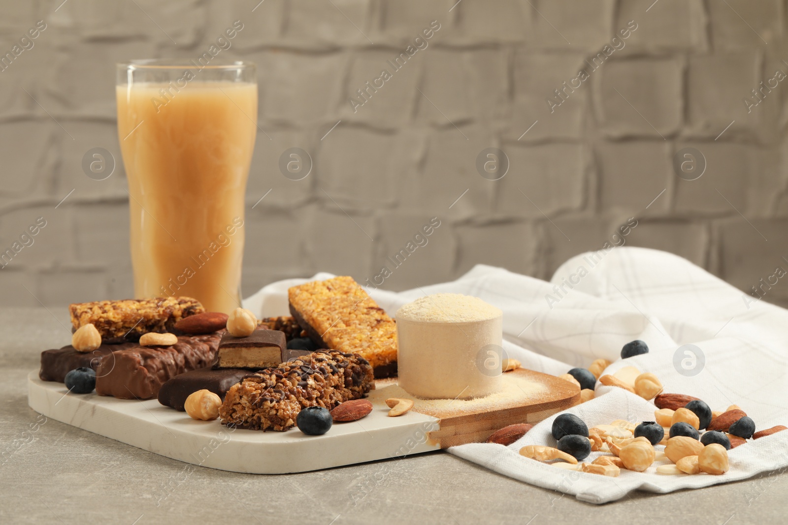 Photo of Different energy bars, nuts, blueberries, protein cocktail and powder on grey table
