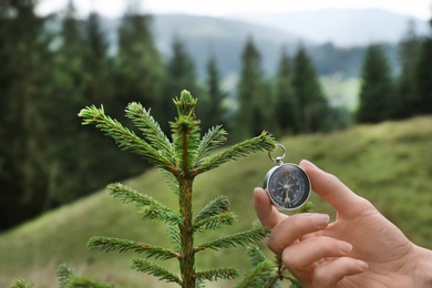 Woman checking modern compass in wilderness, closeup