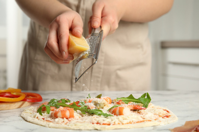 Photo of Woman grating cheese onto pizza at white marble table, closeup
