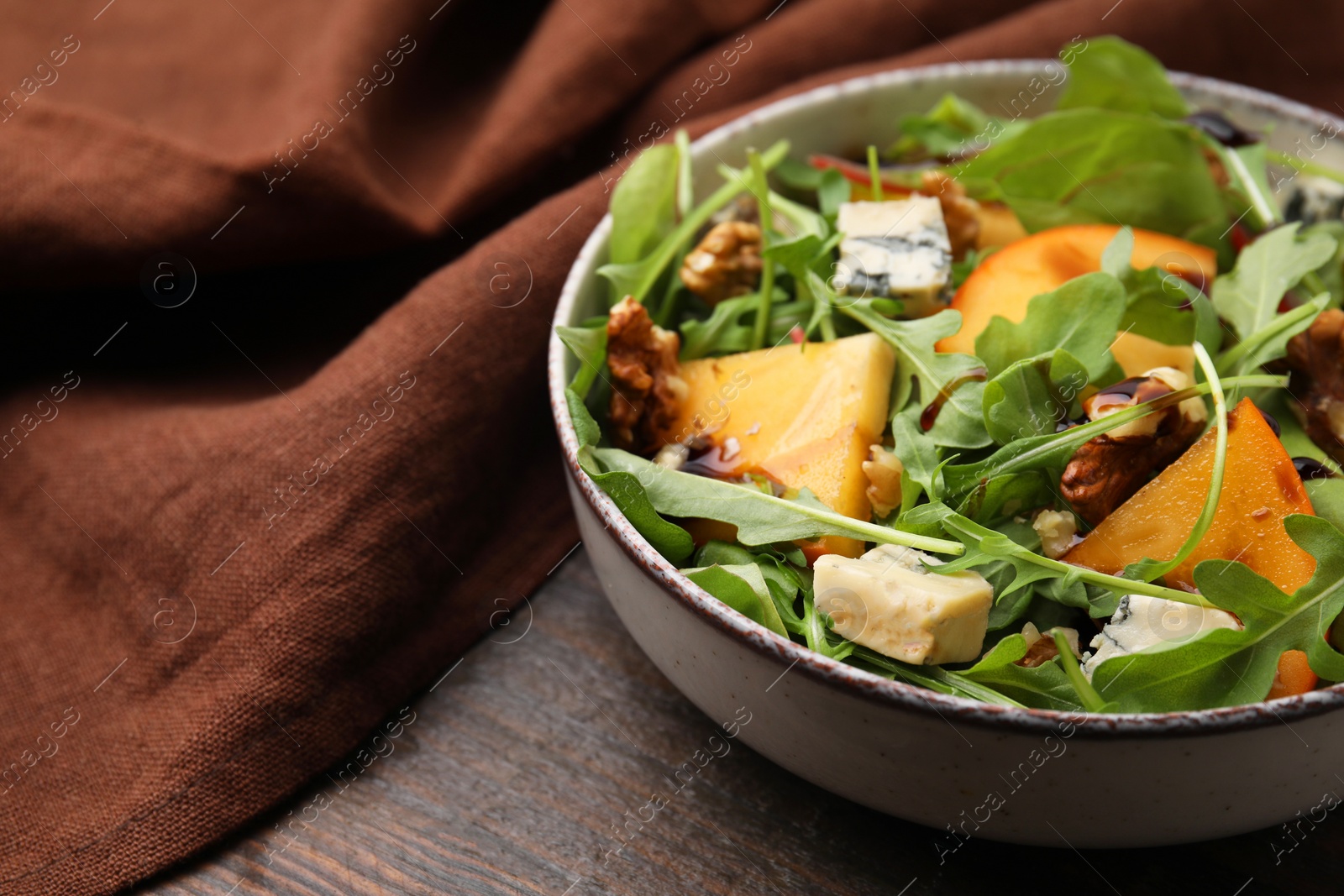 Photo of Tasty salad with persimmon, blue cheese and walnuts served on wooden table, closeup. Space for text