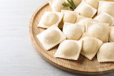 Uncooked ravioli and rosemary on white wooden table, closeup